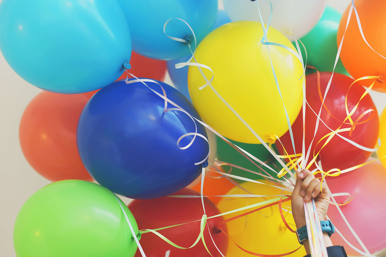 Ein Kind hält viele bunte Luftballons in der Hand.