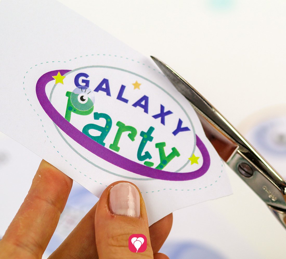 Die einzelnen Motive der balloonas Weltraum Geschenkaufkleber, zum Beispiel ein Planet mit der Aufschrift Galaxy Party,  werden entlang der Linie ausgeschnitten.